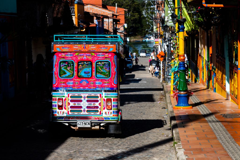 A lively, colorful chiva bus on a sunlit street in Guatapé, Colombia showcasing vibrant urban life.
