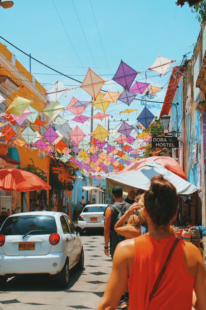 Tourists walk under colorful kites in a vibrant street of Cartagena, Colombia, capturing the lively urban atmosphere. Things to know before traveling to colombia