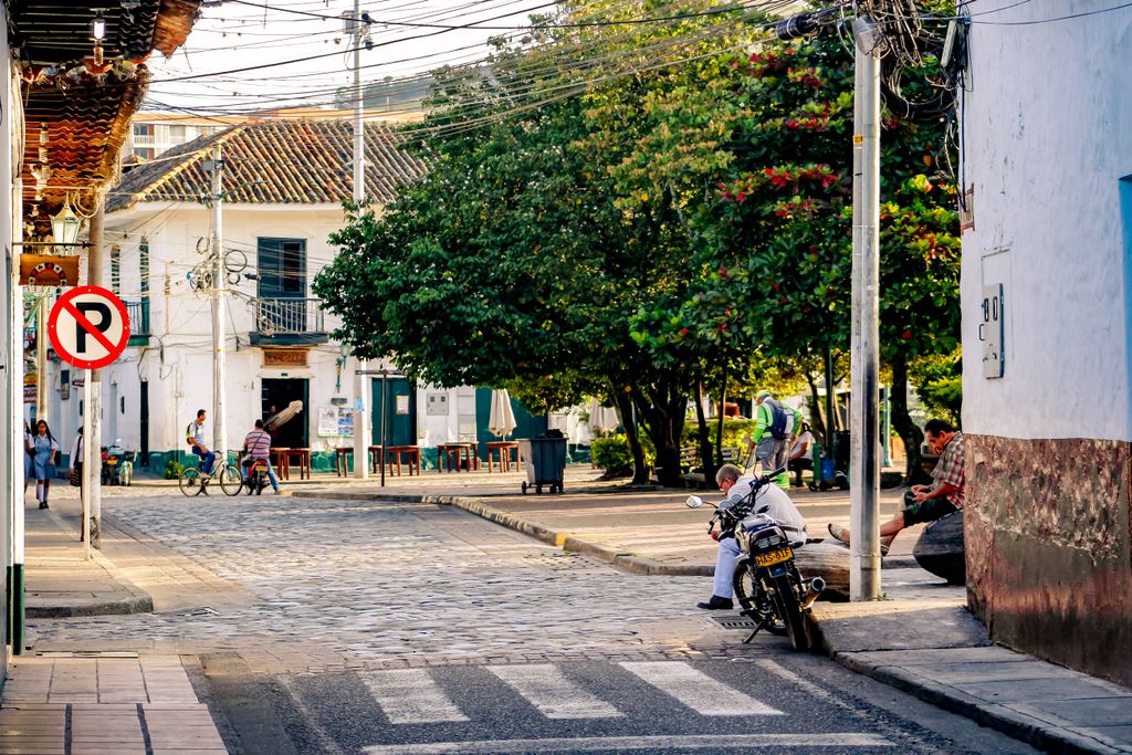 Vibrant street scene in a Latin American town featuring people, trees, and a bustling atmosphere.