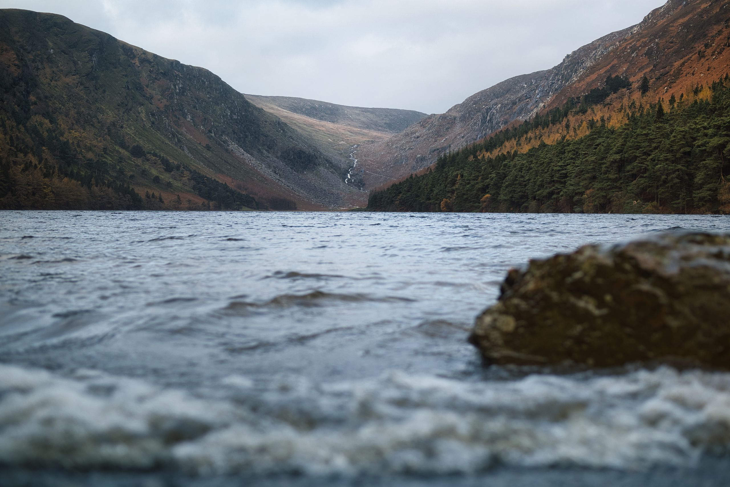 Breathtaking view of a lake surrounded by mountains in Ireland with a distant waterfall.