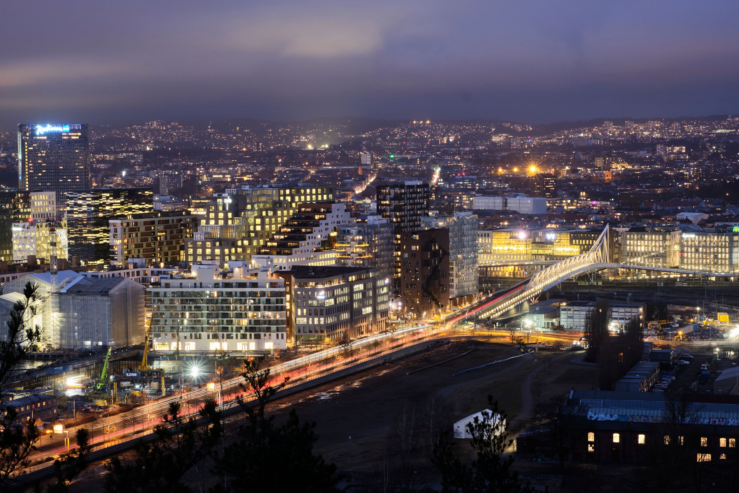 Captivating cityscape featuring illuminated buildings, a bridge with light trails, captured at twilight in an urban setting.