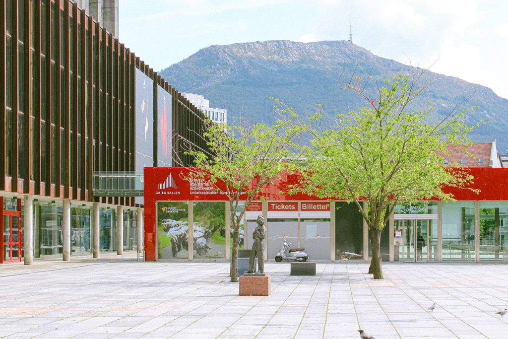 Exterior view of Grieghallen in Bergen, Norway, against a mountain backdrop. A tranquil town square scene.