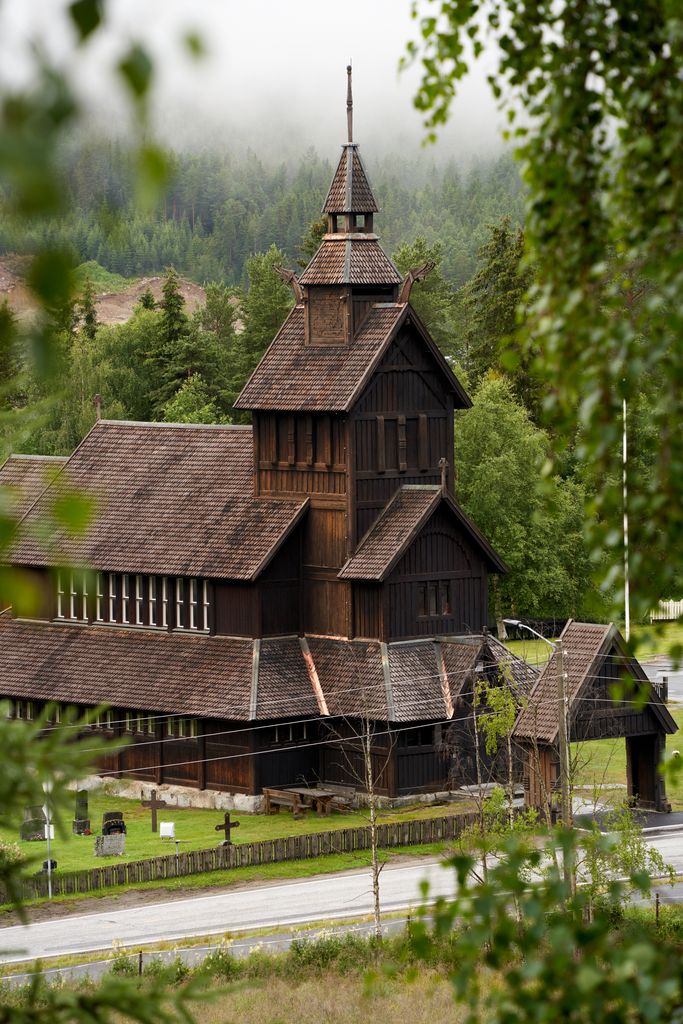 Historic wooden church in Uvdal, Norway surrounded by lush greenery and misty hills.