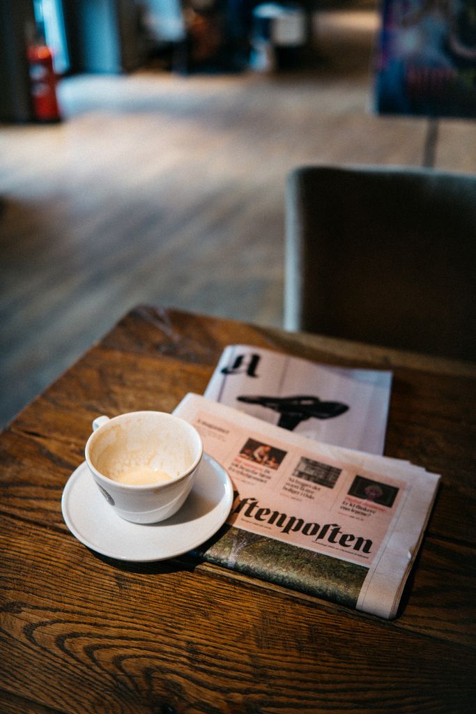A warm, inviting coffee cup with a newspaper on a wooden table in a cozy cafe setting.