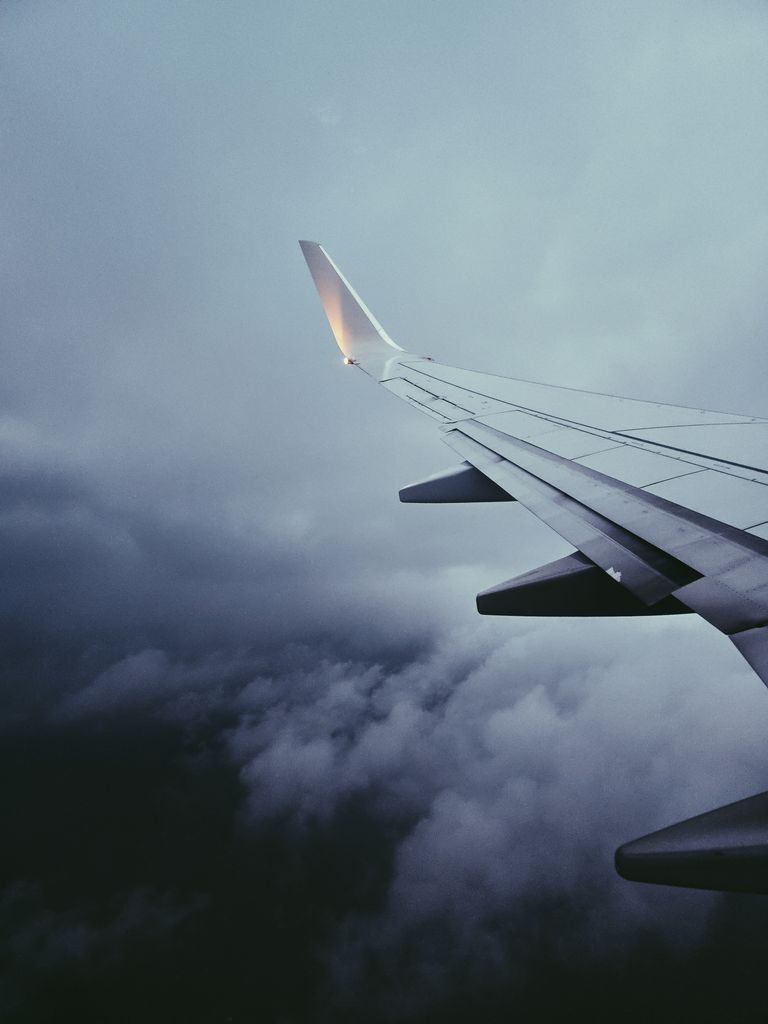 View of an airplane wing flying through dramatic cloudy skies, showcasing a serene mid-flight moment.